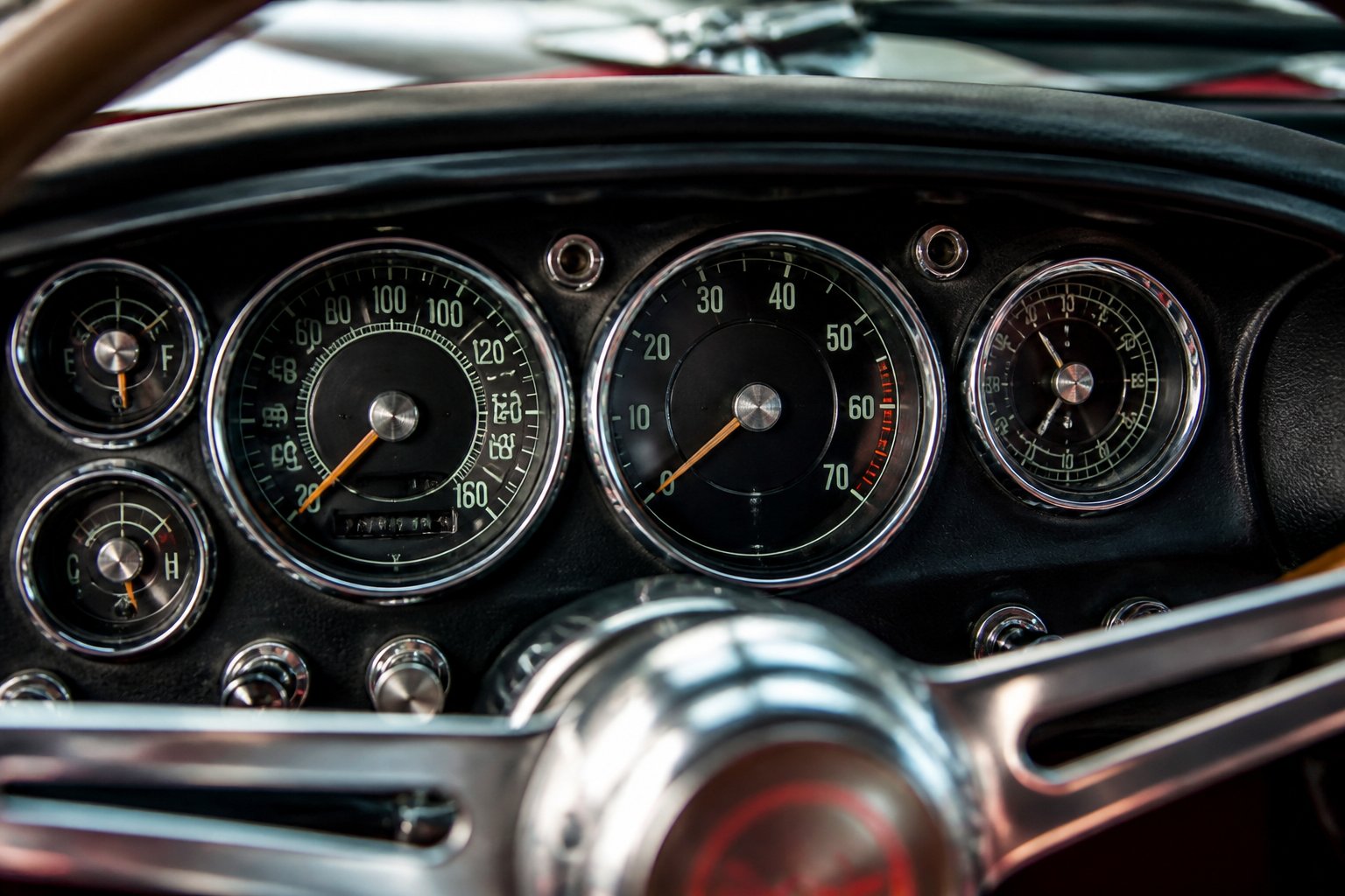 Close-up view of a classic car's analog dashboard with round chrome bezels around the gauges.