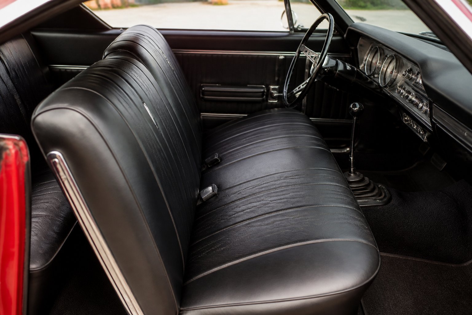 Front bench seats inside a classic 1960s muscle car with vintage leather upholstery and a retro dashboard.