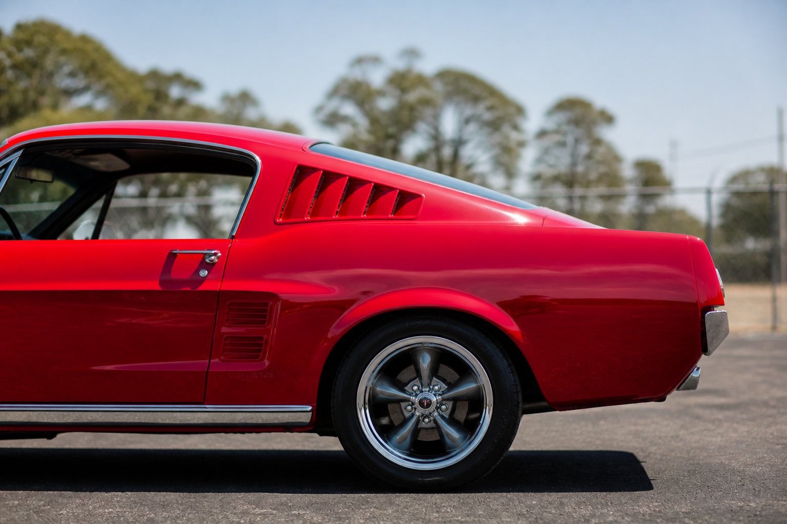 Side view of a classic 1960s muscle car with a fastback roofline parked outdoors on a sunny day.