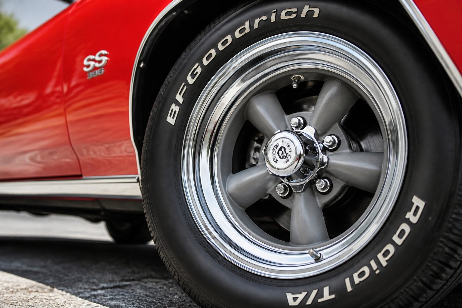 Close-up of polished vintage muscle car wheels with mag-style magnesium and steel rims on a red car outdoors.