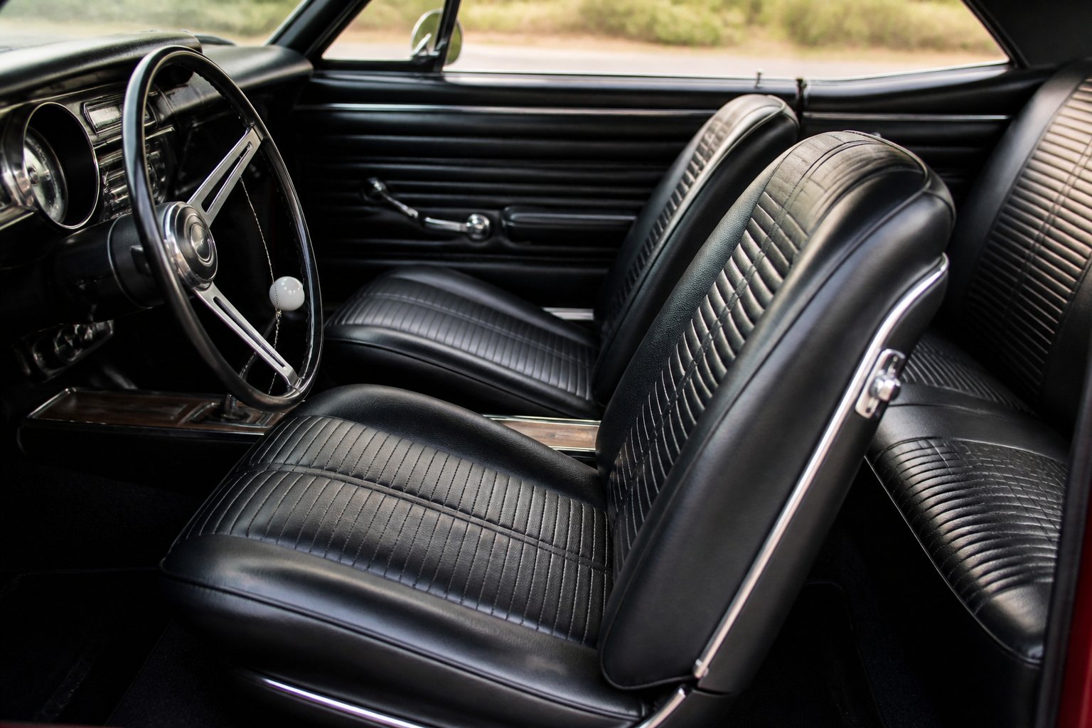 Interior view of a 1960s muscle car showing lightweight vinyl bucket seats and part of the dashboard.