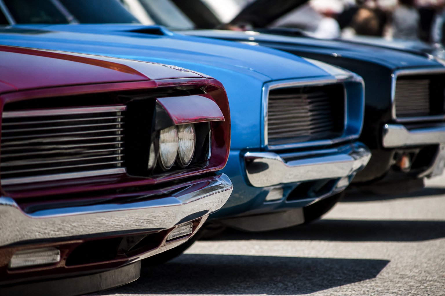 Close-up of front grilles and hidden headlights on classic 1960s muscle cars parked side by side.