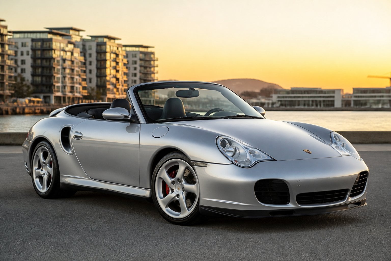 A silver Porsche 911 Turbo Cabriolet with the top down parked outdoors in an urban setting.