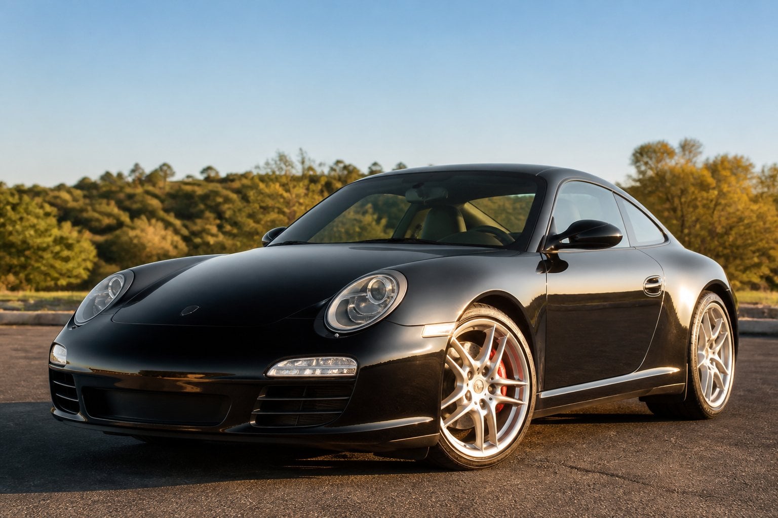 A Porsche 911 Carrera (997) S parked outdoors on a smooth surface with greenery and sky in the background.