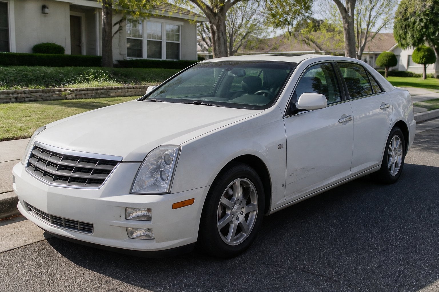 A late 2000s Cadillac STS parked on a suburban street with a dim dashboard light visible through the windshield.