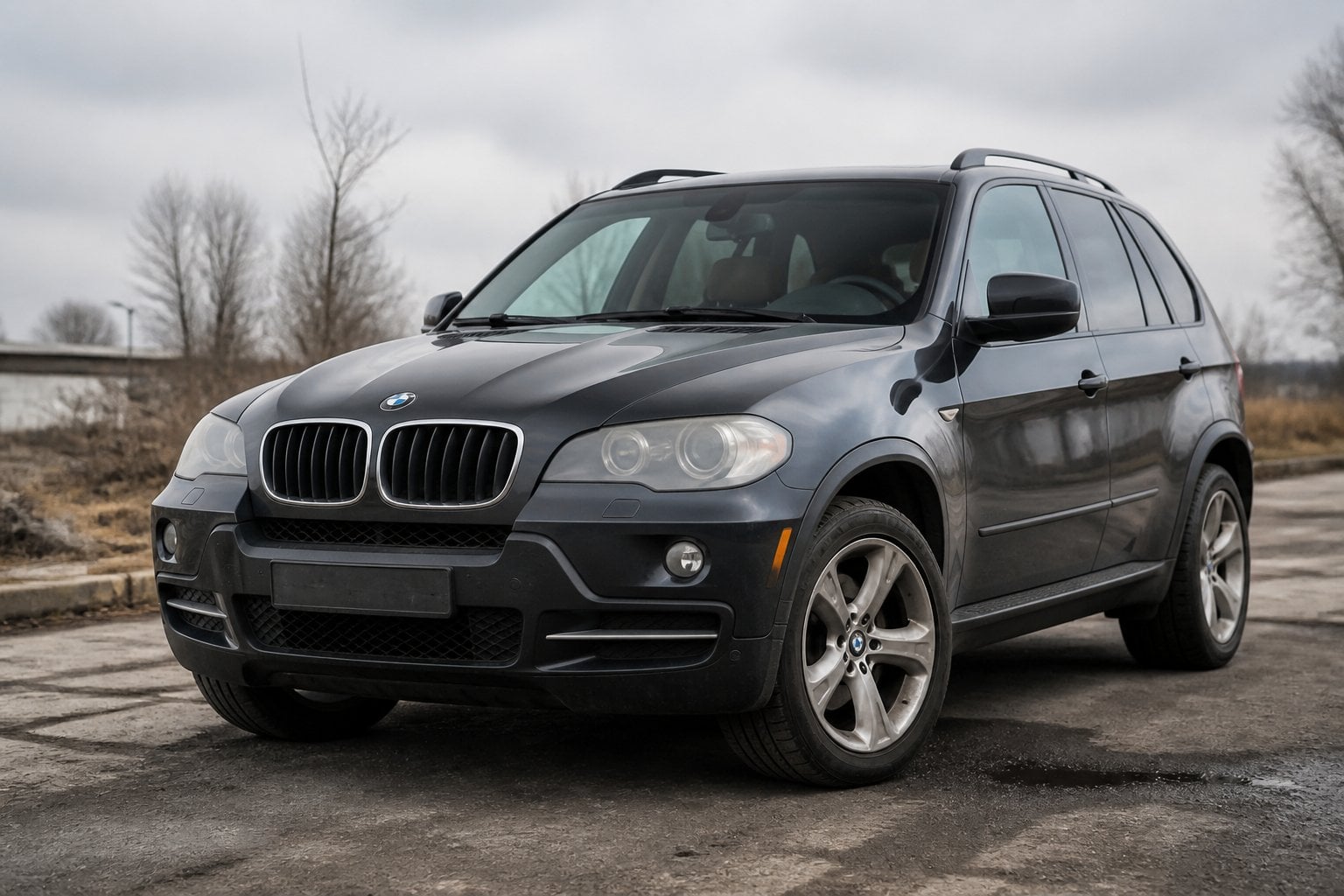 A dark gray BMW X5 SUV parked in an aging roadside lot.