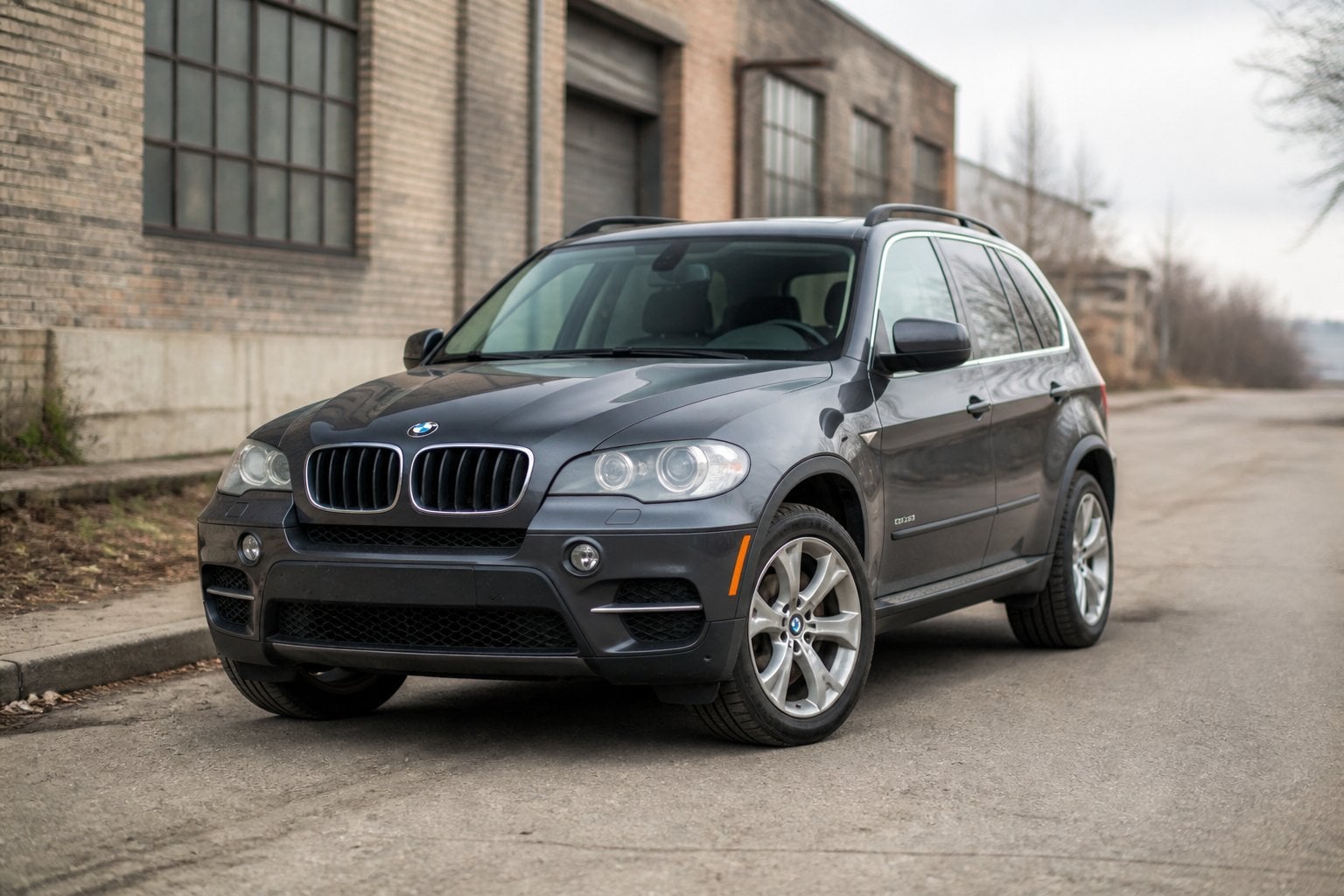 A dark gray BMW X5 SUV parked on an aging urban roadside.
