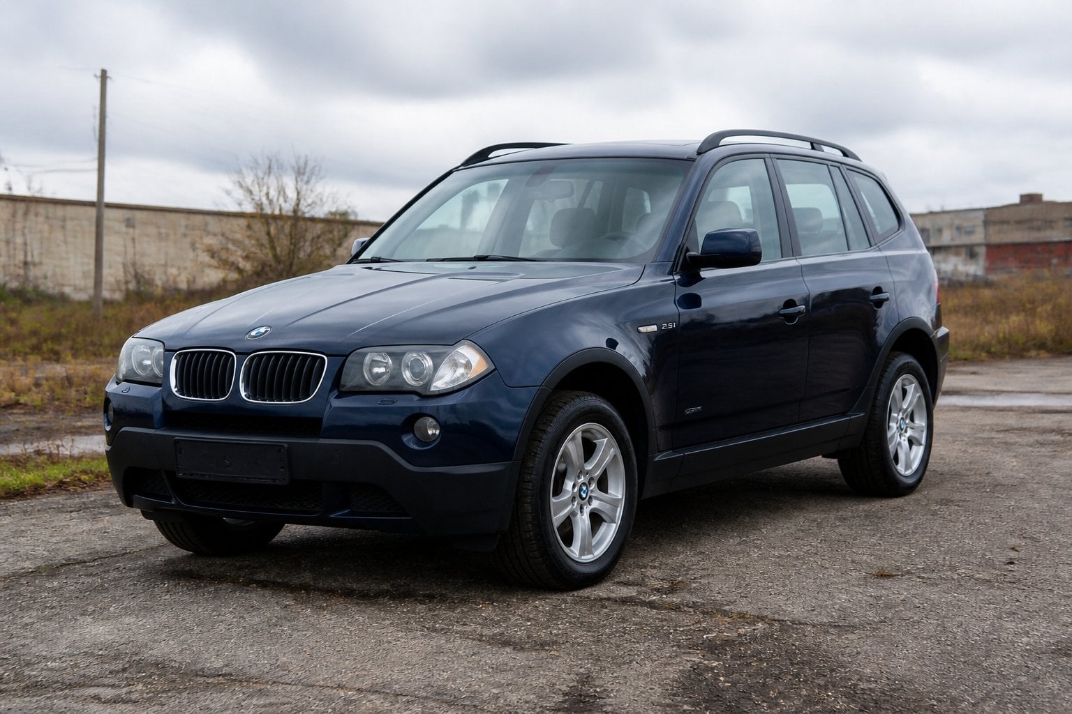 A dark blue BMW X3 SUV parked on a worn roadside near an industrial area.