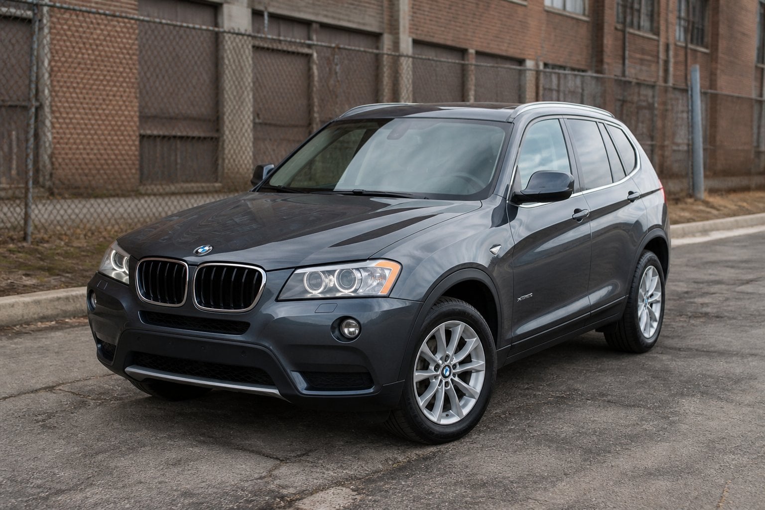 A BMW X3 SUV parked on a quiet roadside near an industrial area.