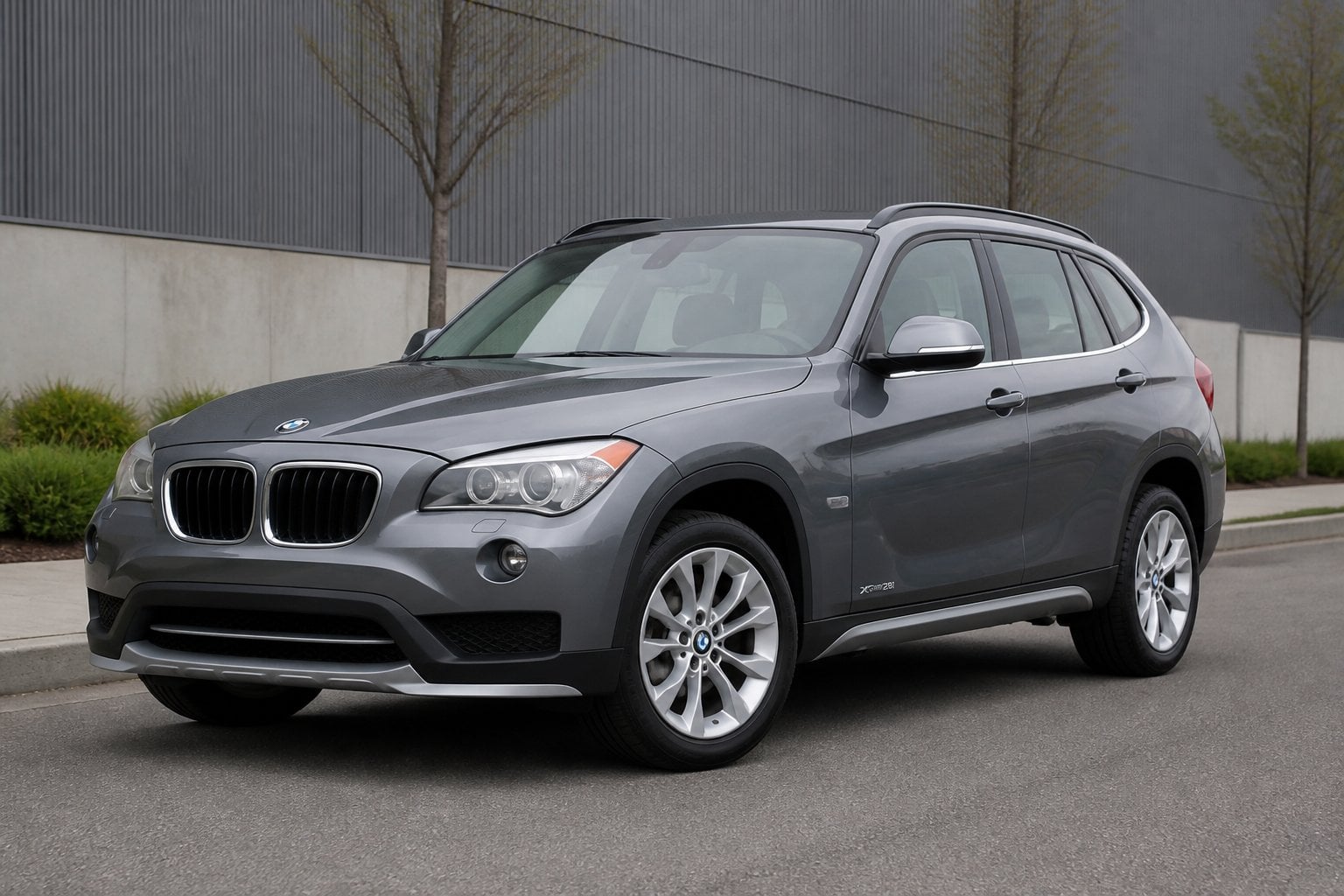 A gray BMW X1 compact SUV parked on a paved road near an urban-industrial setting.