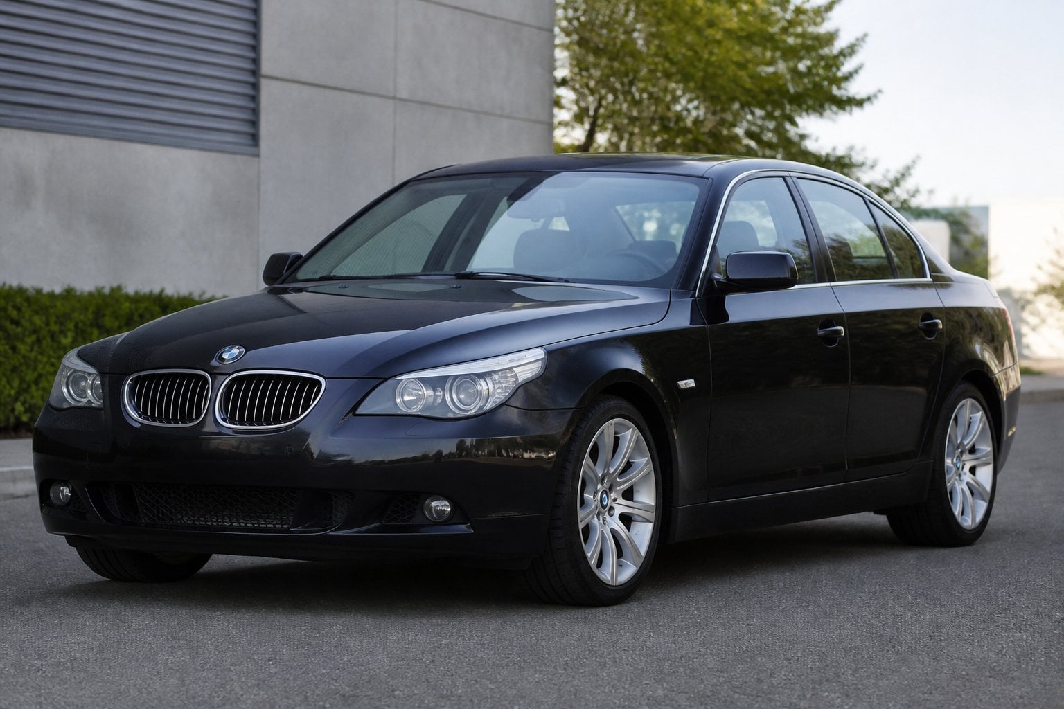 A dark gray BMW 5 Series E60 sedan parked on a quiet roadside, viewed from the front at an angle.