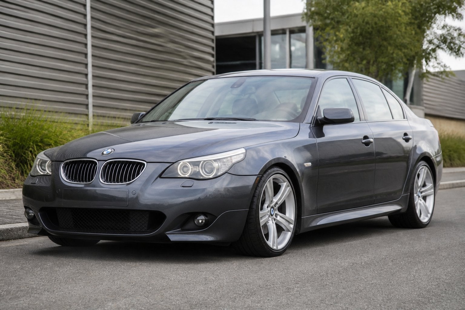 A dark gray BMW 5 Series E60 550i sedan parked on a paved roadside.
