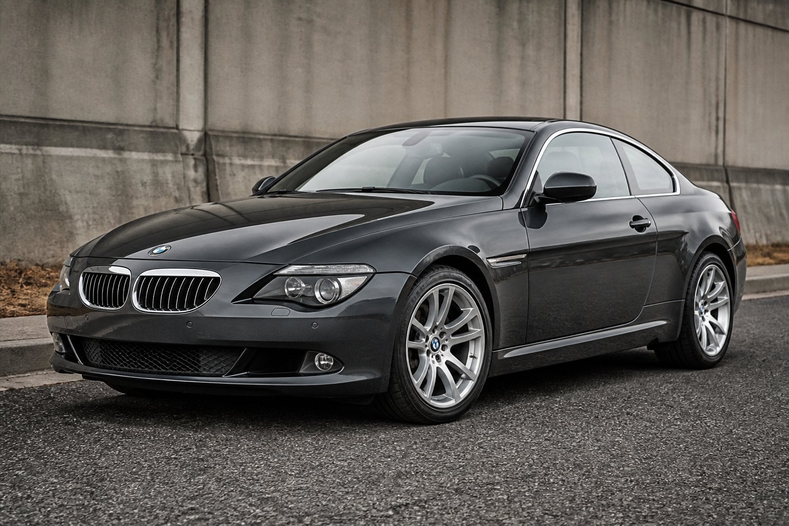 A dark graphite BMW 6 Series E63 650i coupe parked on a quiet urban roadside.