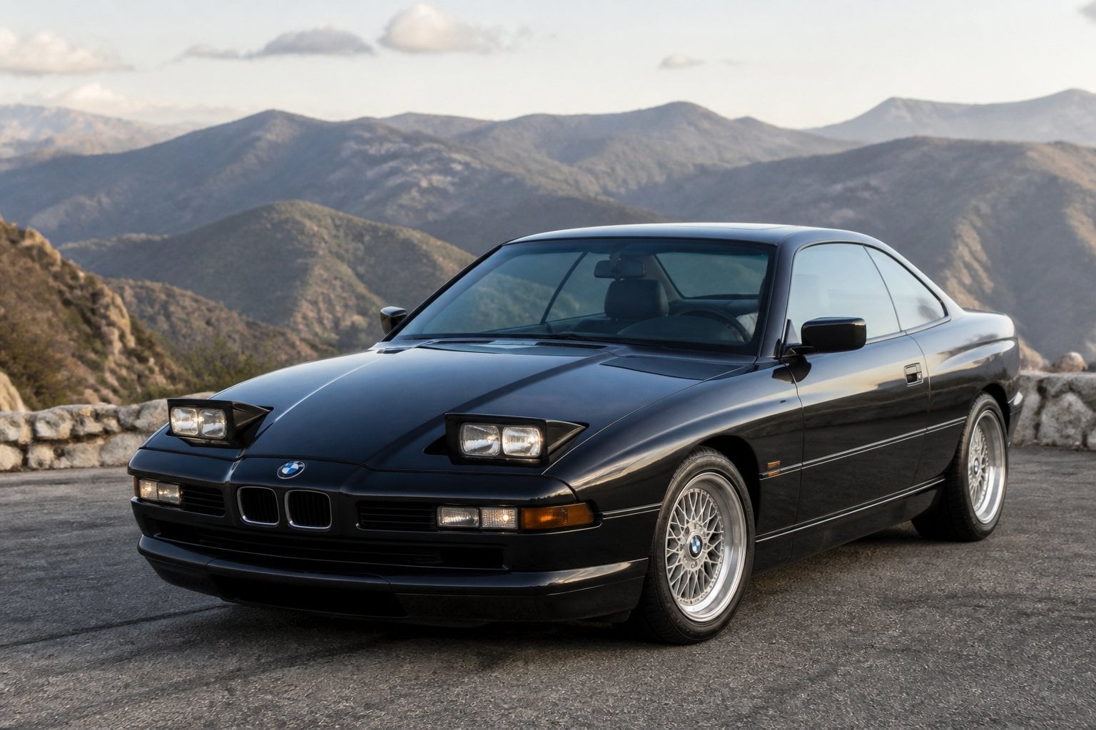 A dark BMW 8 Series E31 coupe parked on a scenic mountain road.