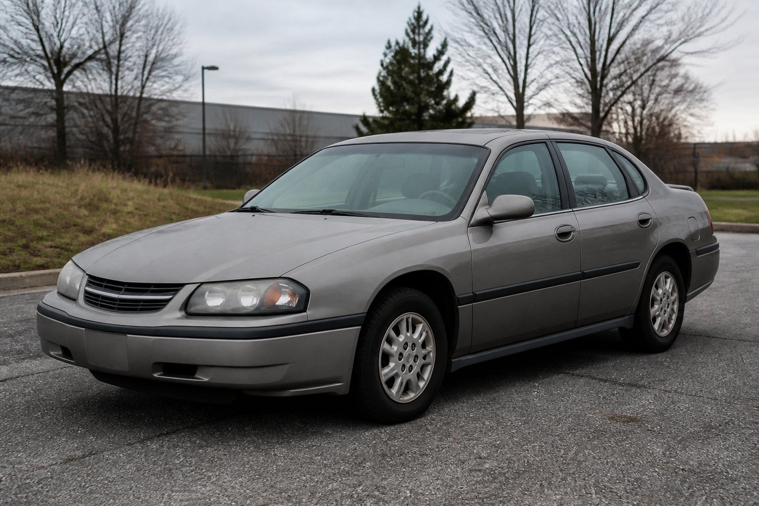A weathered early-2000s Chevrolet Impala sedan parked beside a suburban road.