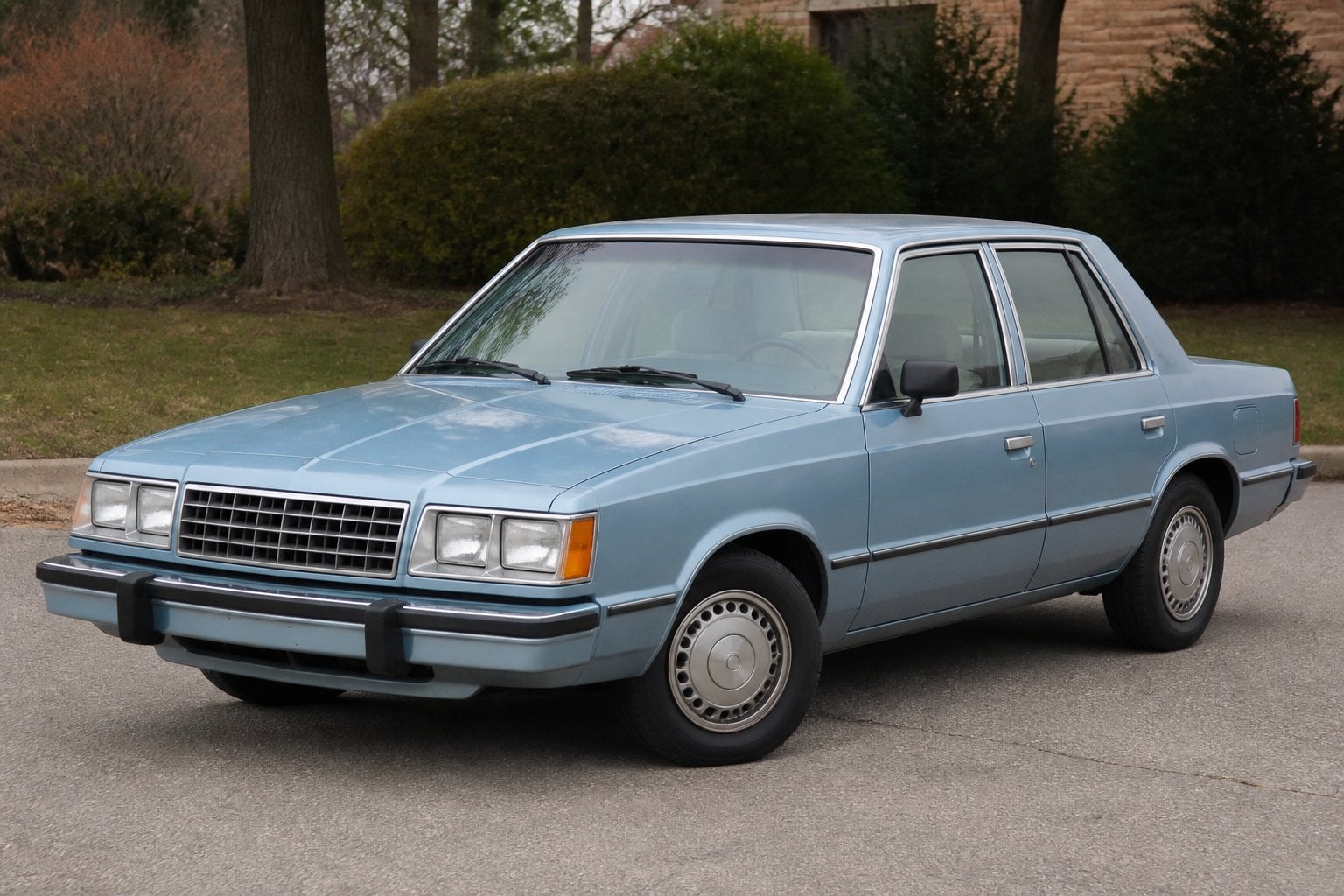A boxy 1980s Dodge Aries sedan parked in a quiet suburban setting.