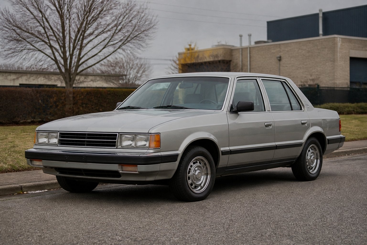 A boxy 1980s Dodge 600 sedan parked on a quiet roadside.
