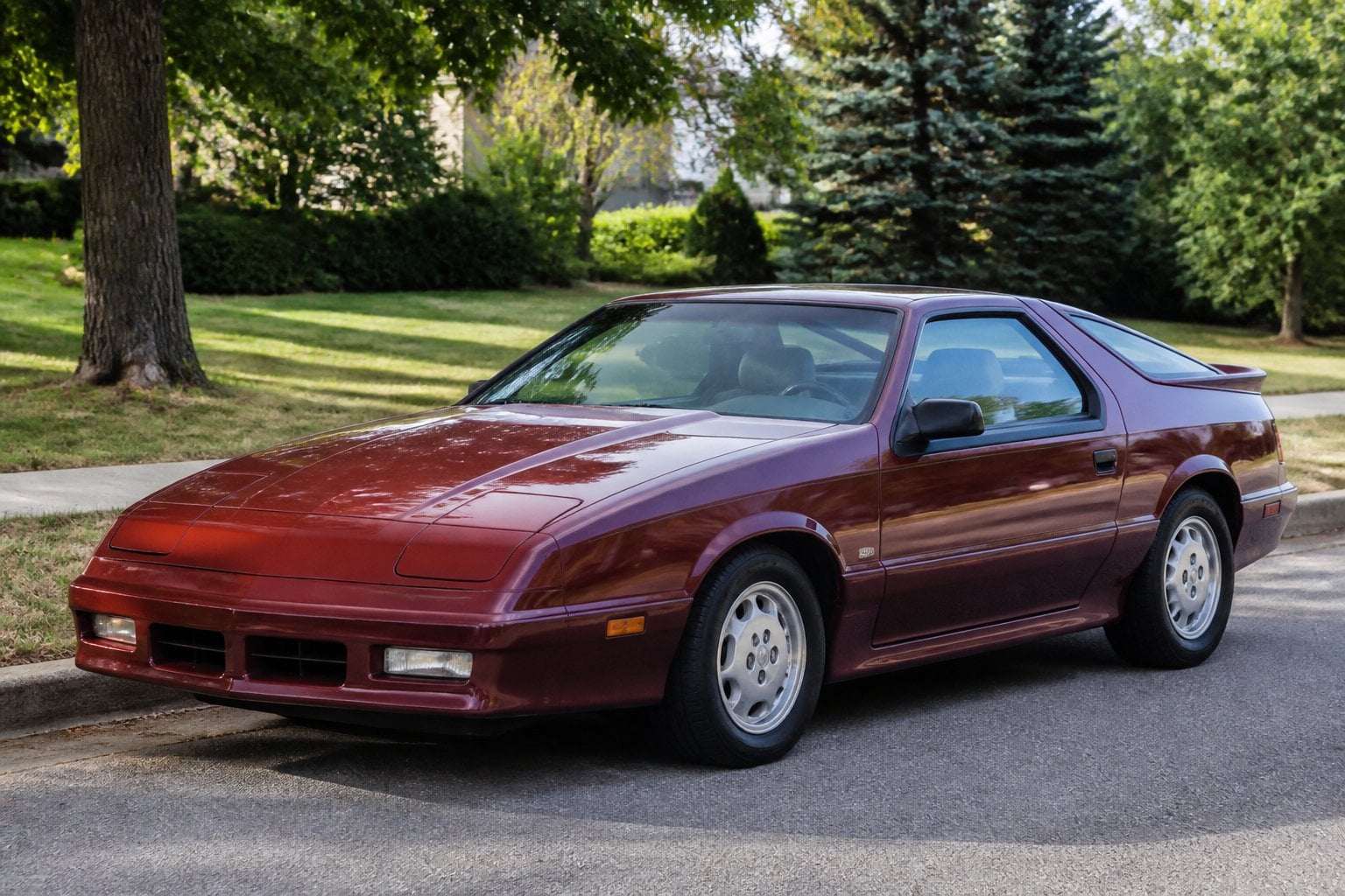 A 1980s Dodge Daytona hatchback parked on a quiet suburban roadside.