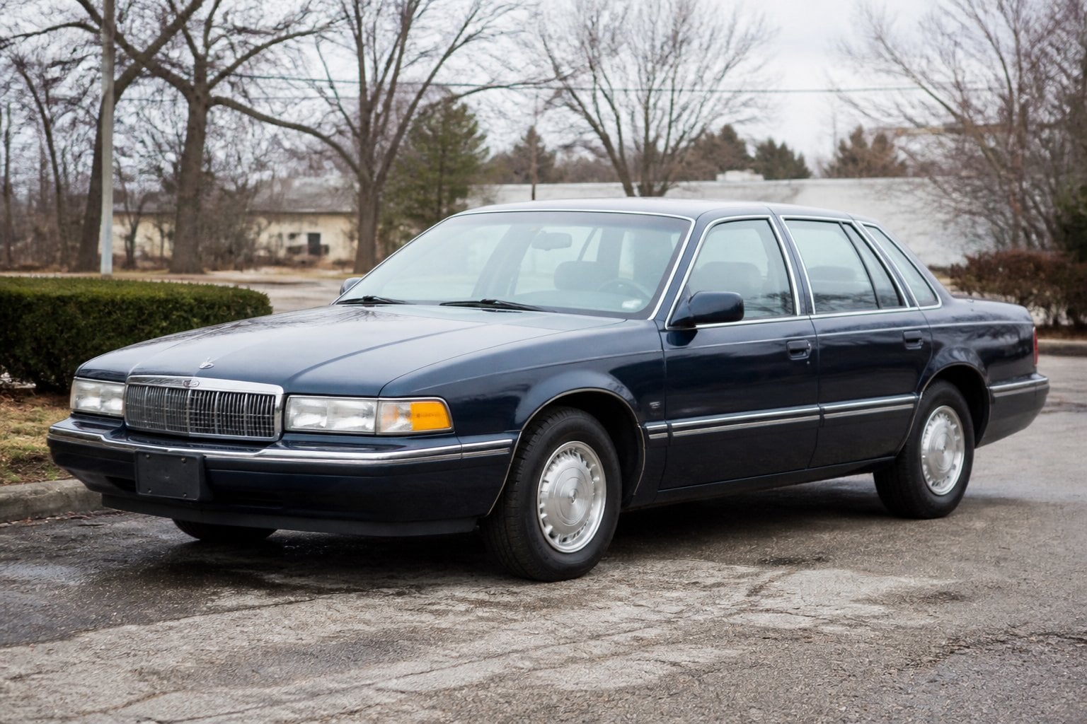 A dark blue early-1990s Dodge Monaco sedan parked beside a quiet roadside.