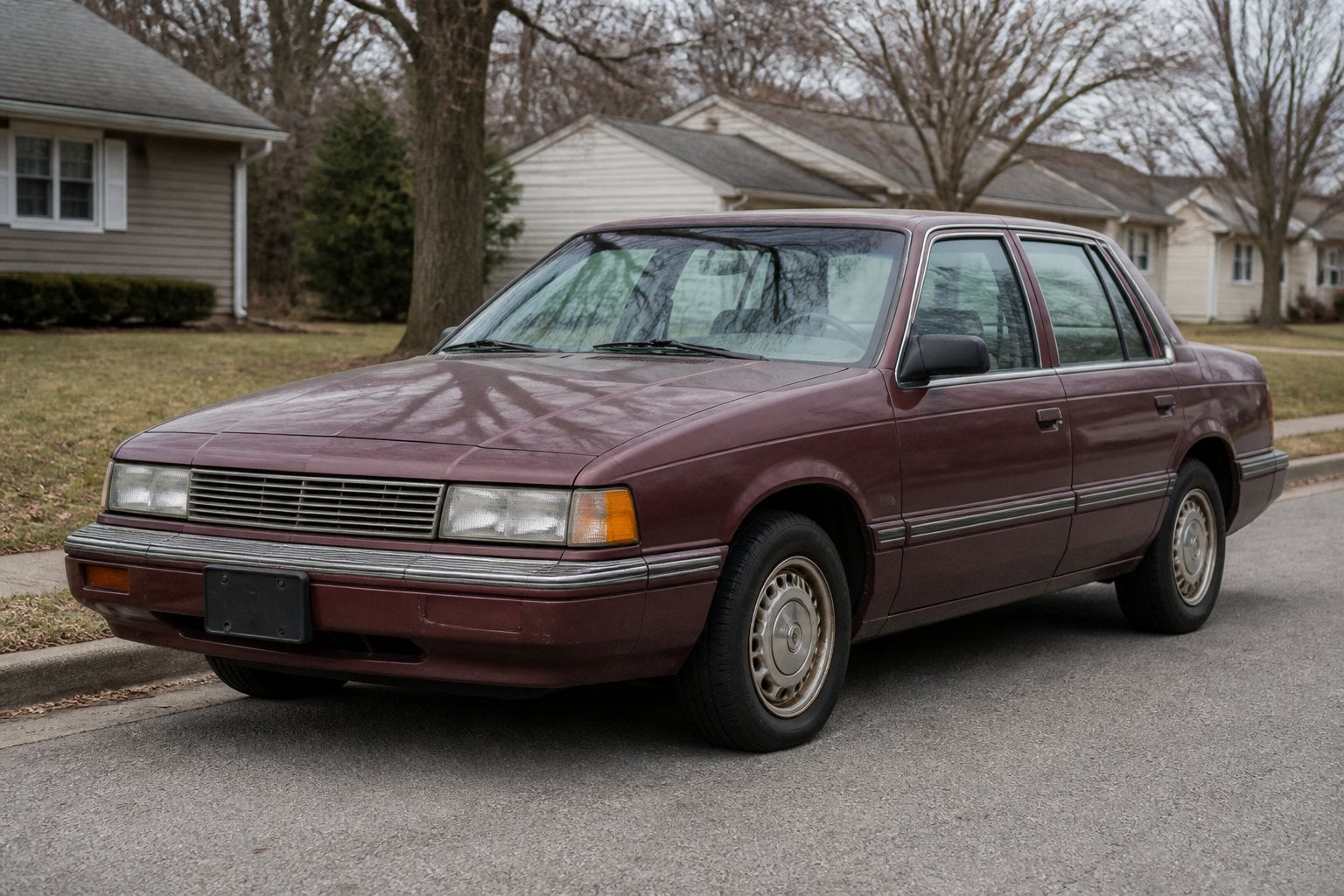 An older boxy four-door Dodge Spirit sedan parked on a quiet suburban roadside.