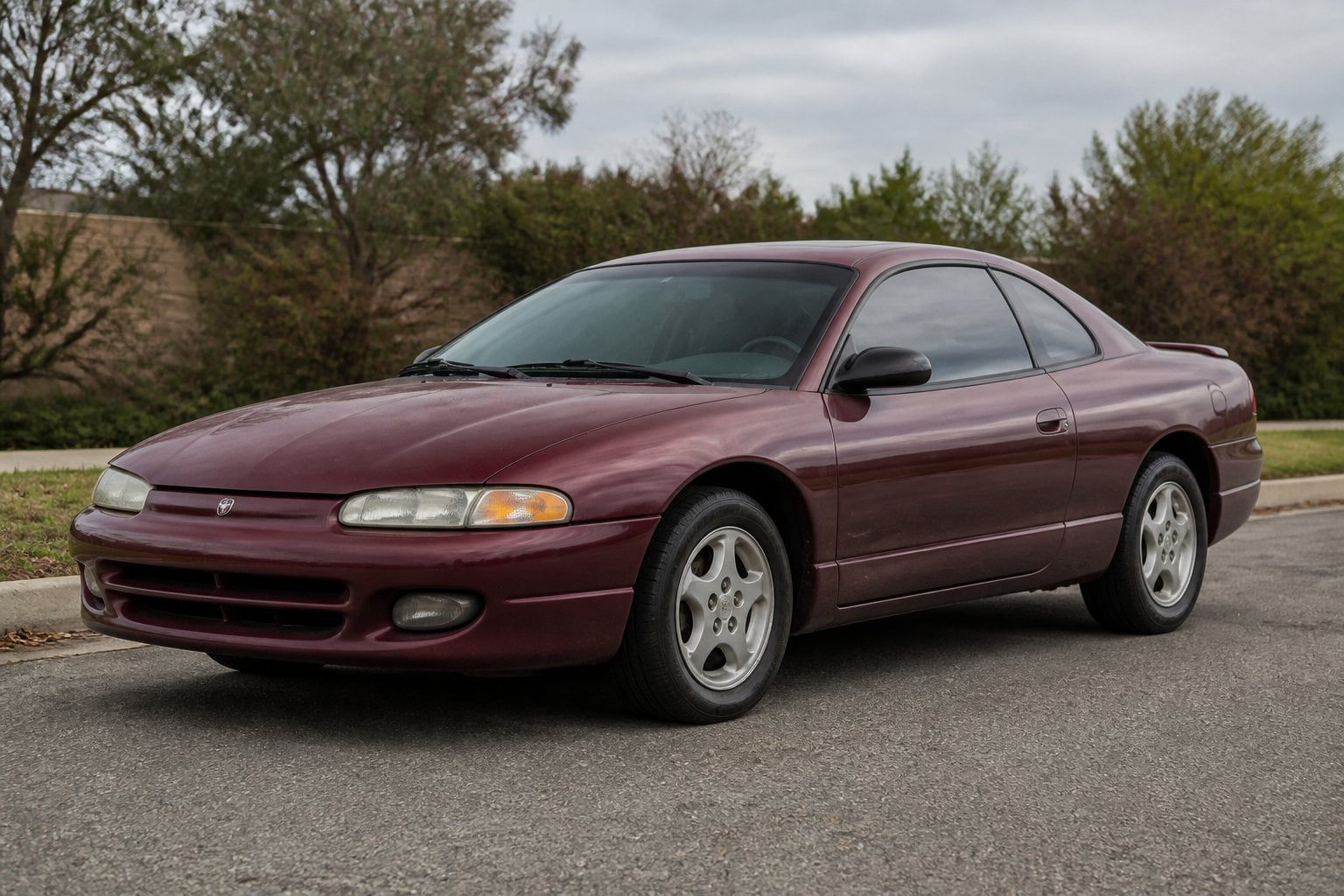 A late-1990s Dodge Avenger coupe parked in a suburban parking lot.