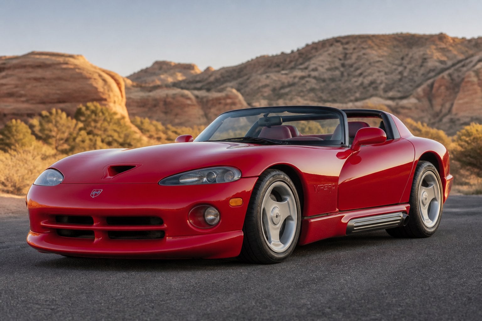 A red first-generation Dodge Viper roadster parked on a paved road in a desert landscape.