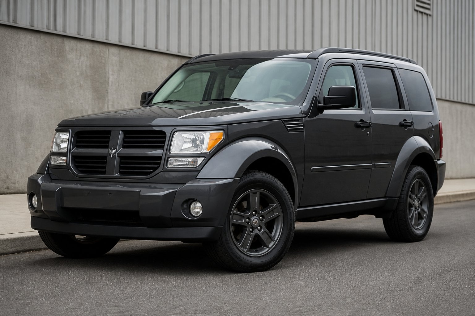 A Dodge Nitro SUV parked on a paved roadside near an industrial area.