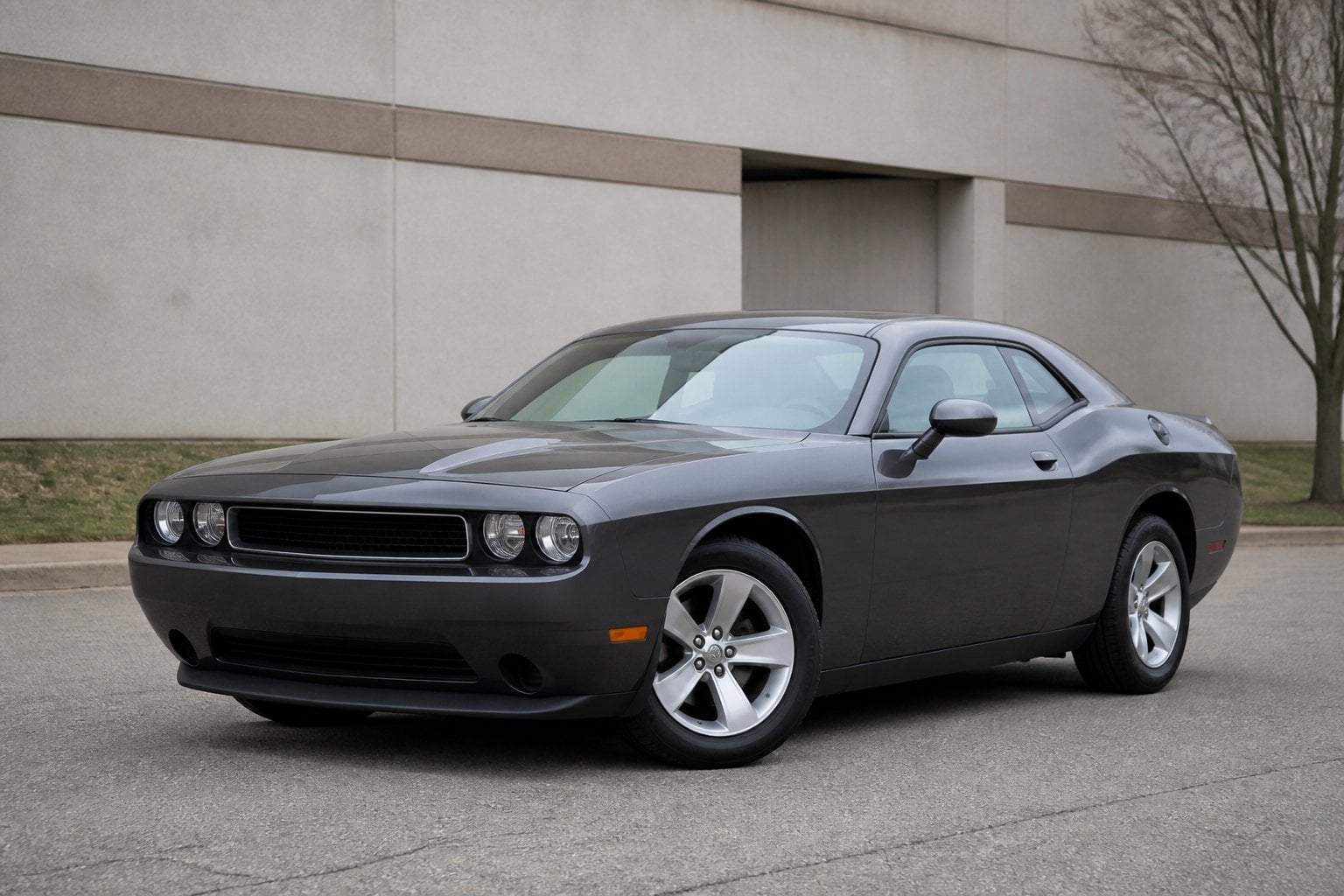 A dark gray Dodge Challenger coupe parked in a quiet industrial lot under overcast skies.