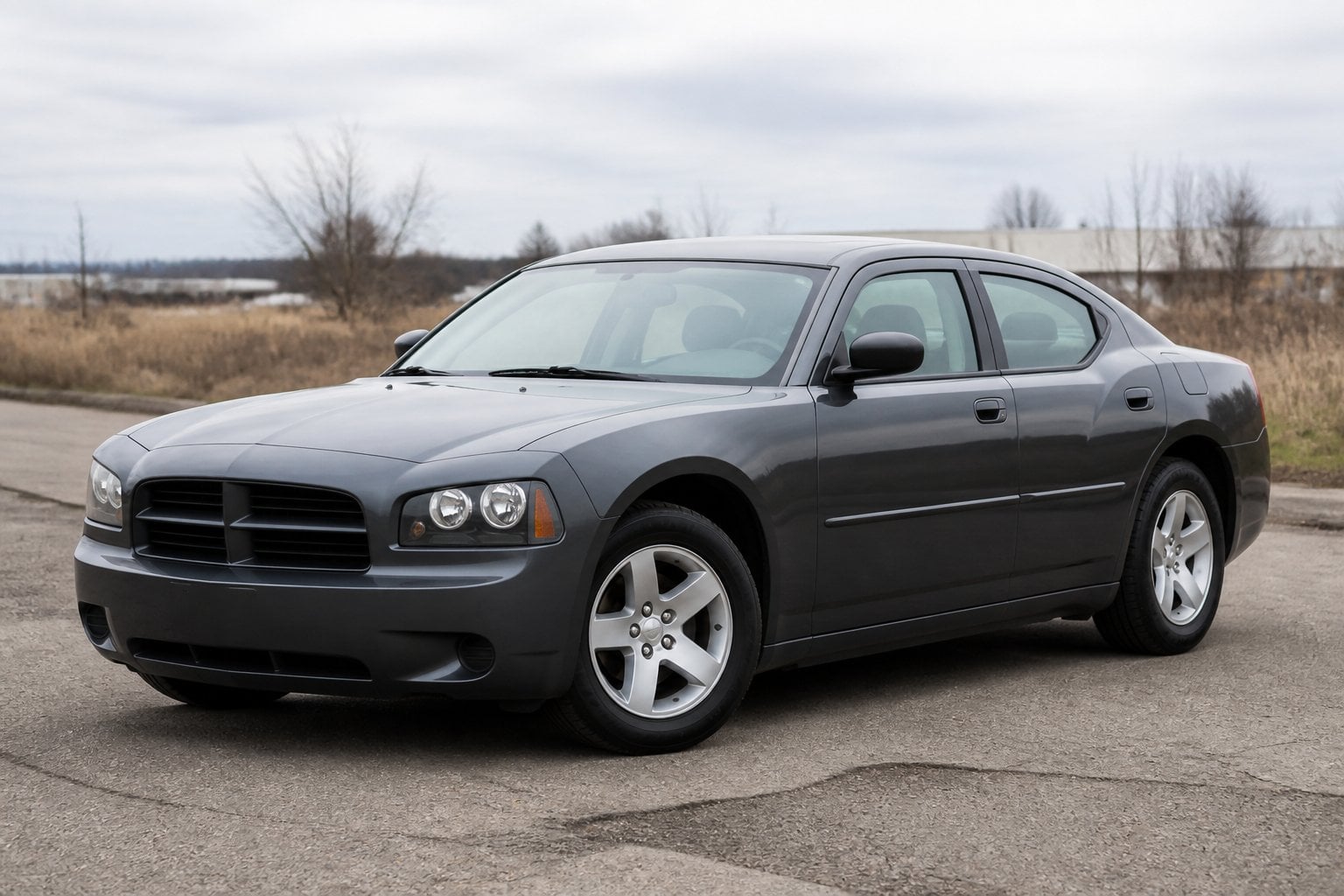 A dark Dodge Charger sedan parked on pavement outside an ordinary roadside setting.