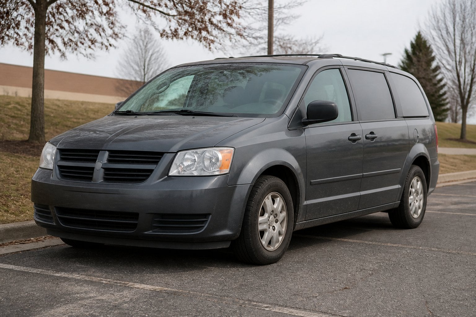 An older dark gray Dodge Grand Caravan parked in a suburban lot on an overcast day.