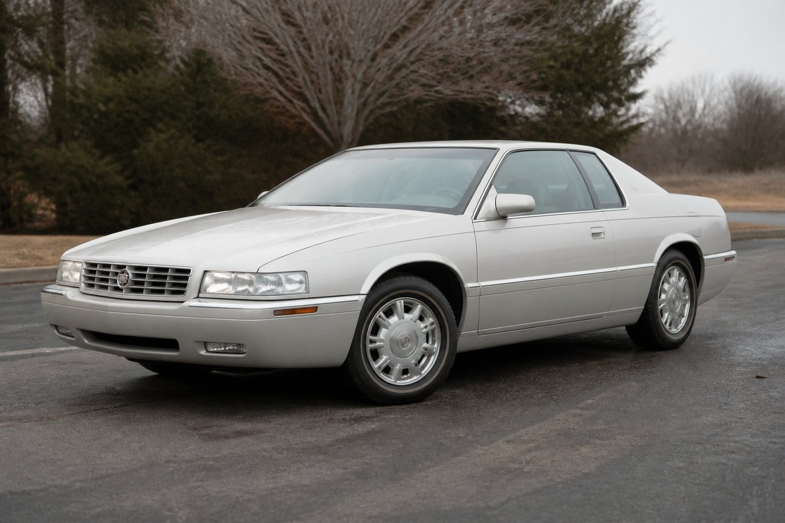 A late-1990s Cadillac Eldorado coupe parked on an asphalt roadside under an overcast sky.