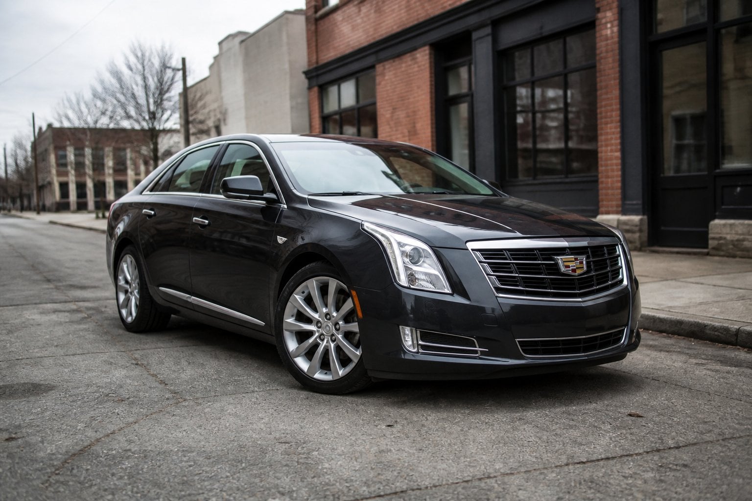 A dark Cadillac XTS sedan parked on a quiet urban roadside.