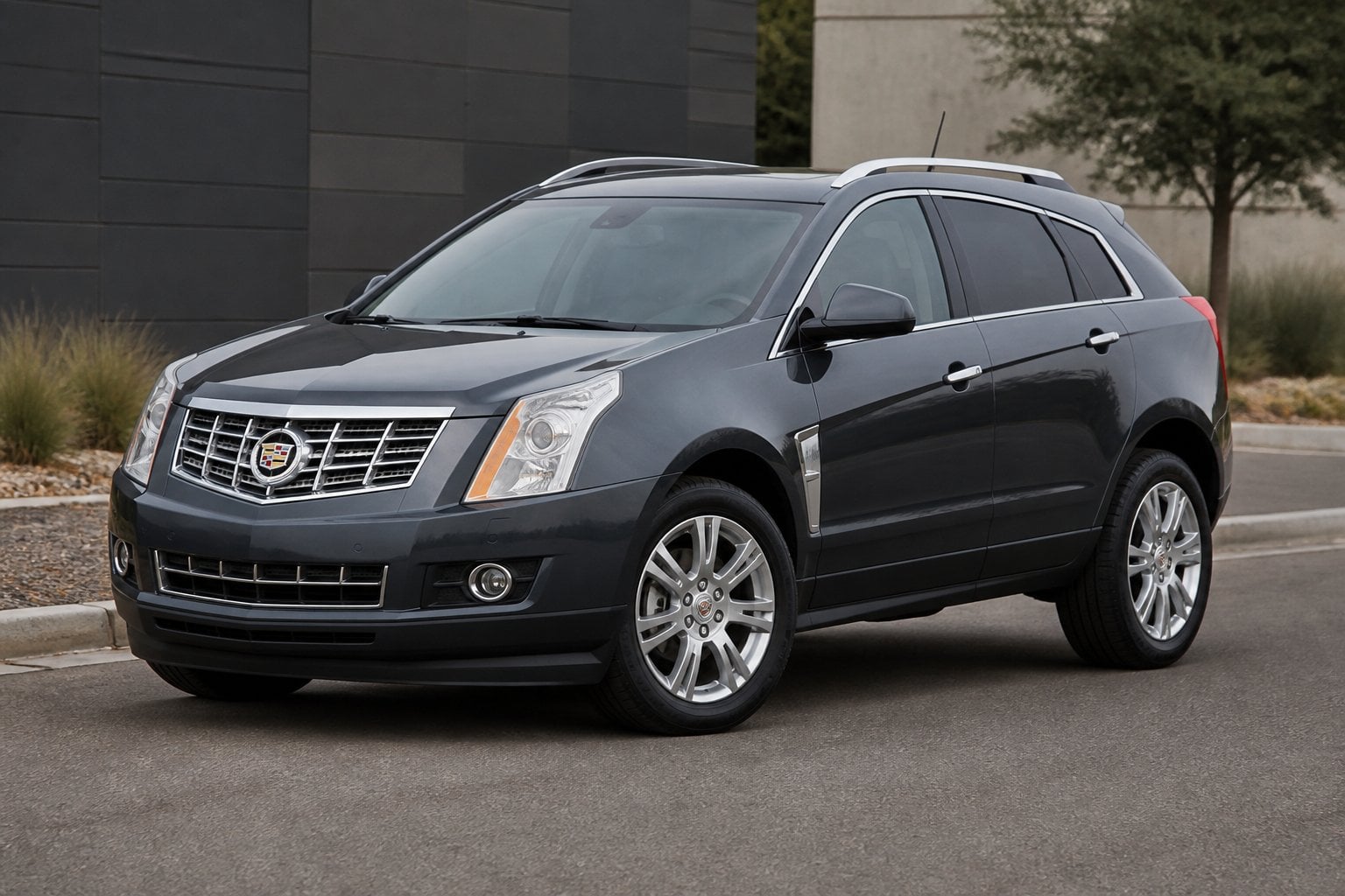 A dark gray Cadillac SRX crossover SUV parked on a quiet suburban roadway.