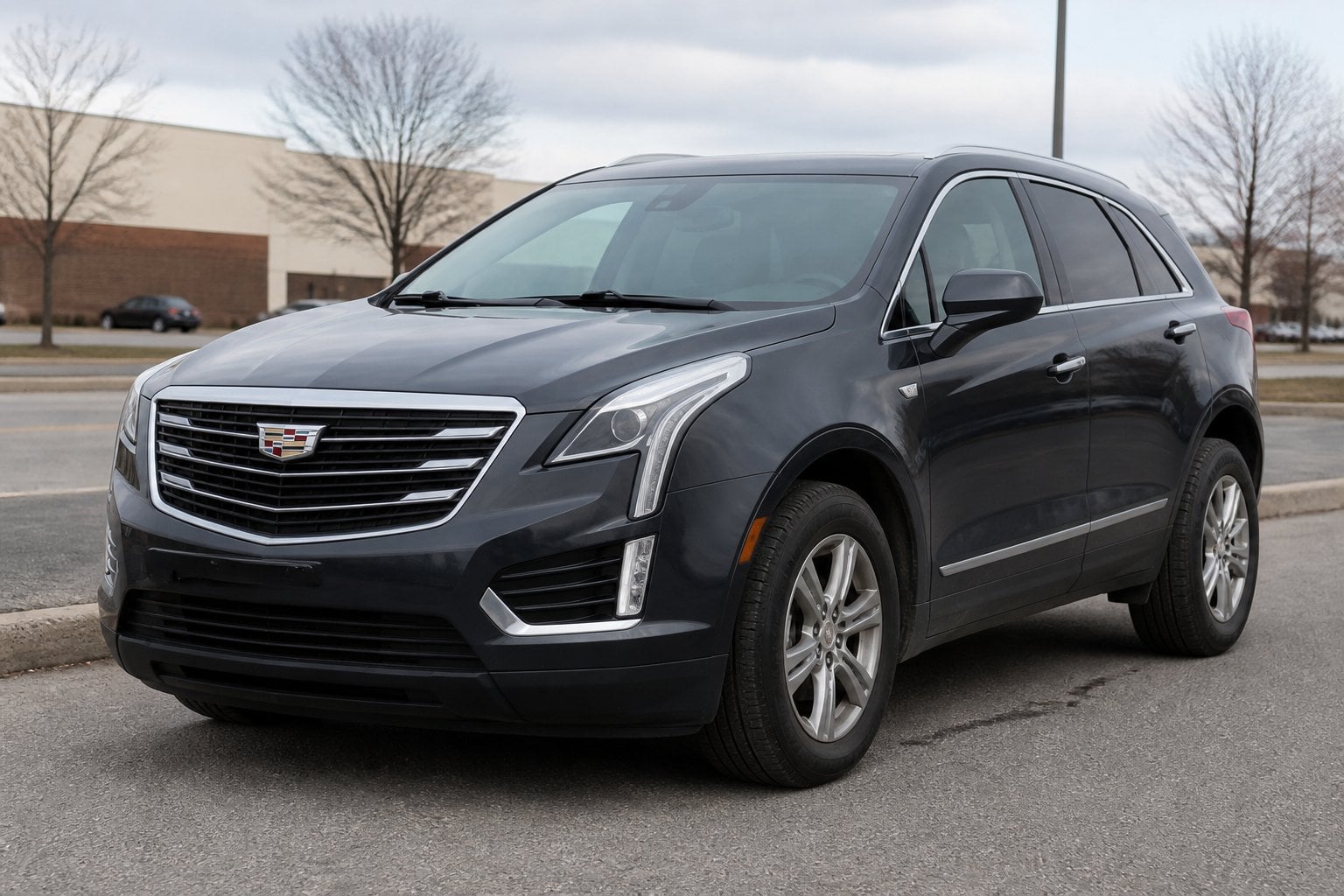 A dark gray early-model Cadillac XT5 SUV parked beside a suburban roadway.