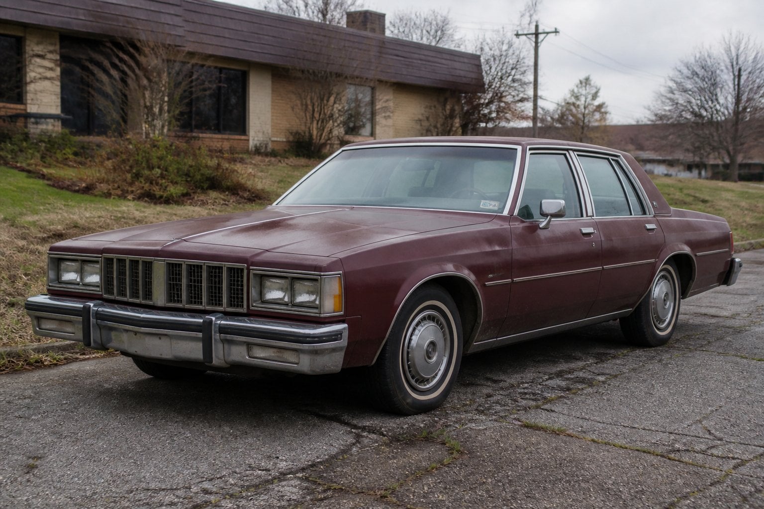An aging boxy Pontiac Parisienne sedan parked beside an overgrown roadside.