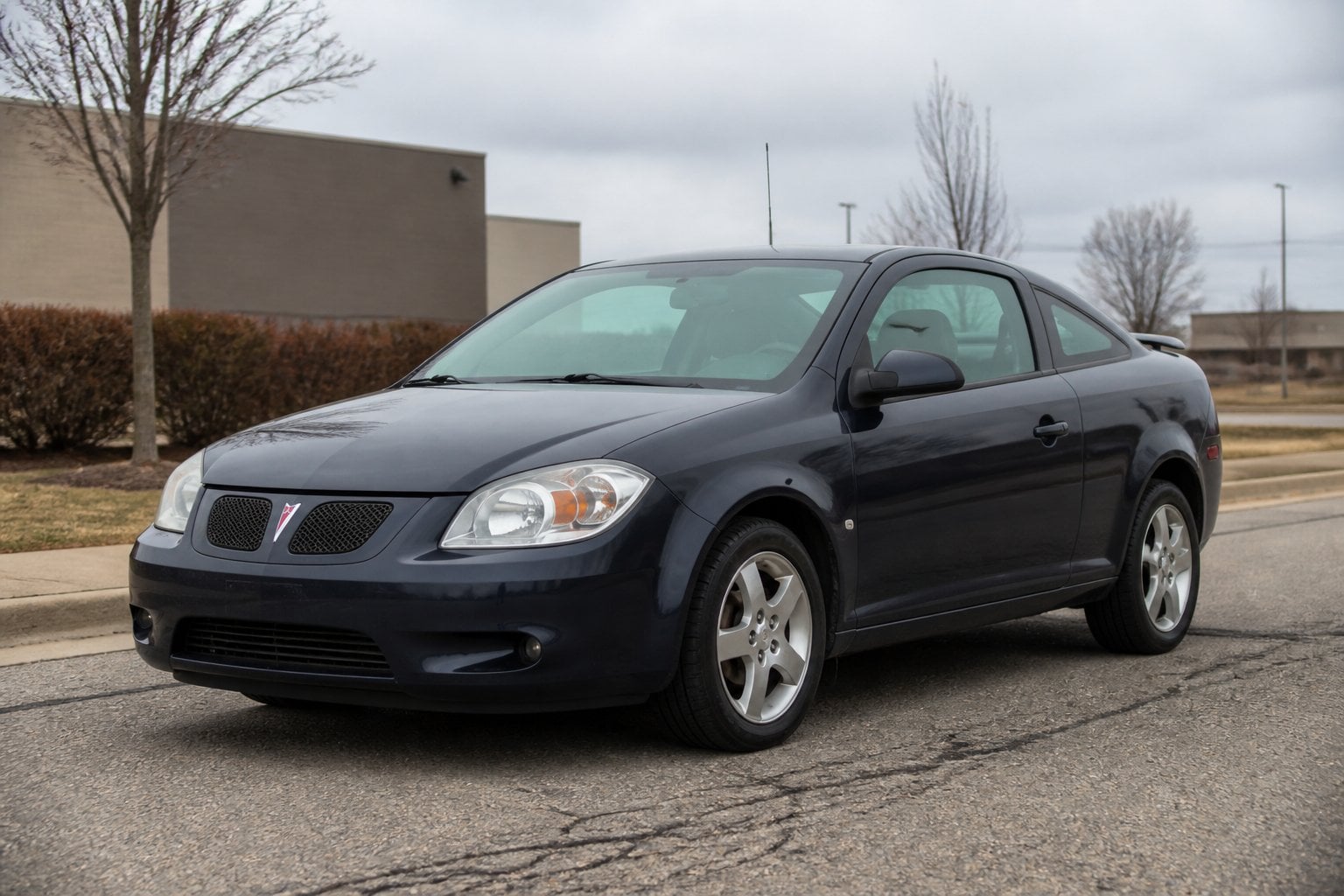 A Pontiac G5 coupe parked on a quiet suburban roadside under an overcast sky.