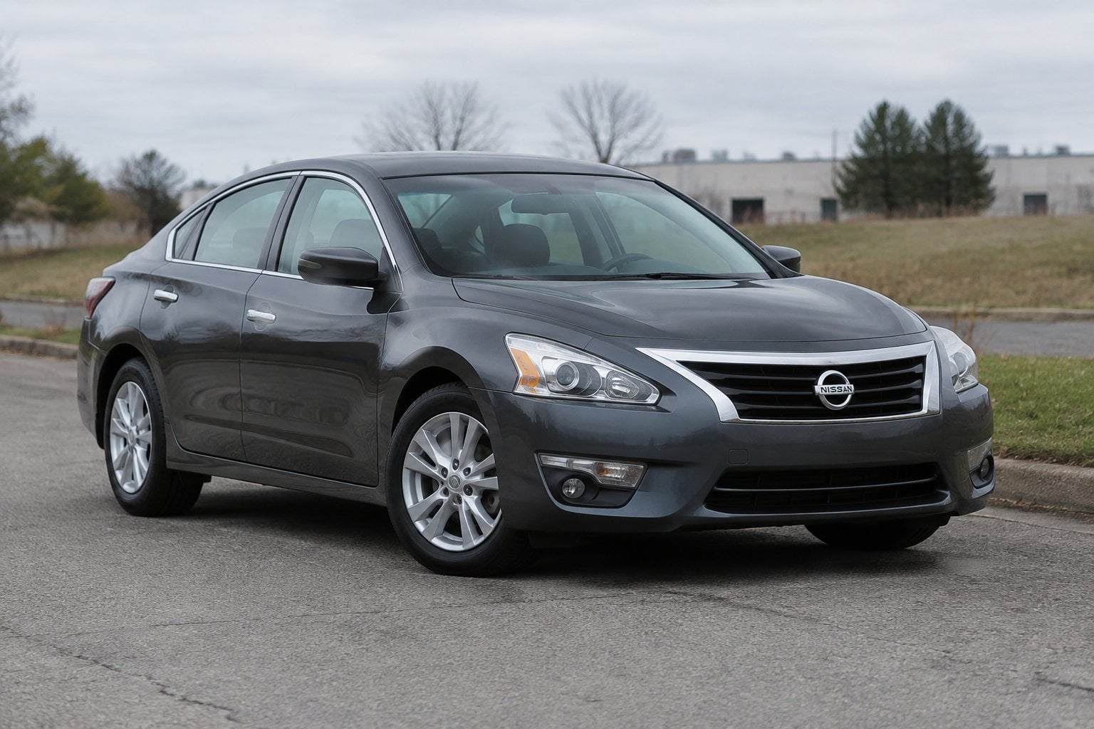 A gray 2013 Nissan Altima parked at a roadside pull-off near suburban buildings.