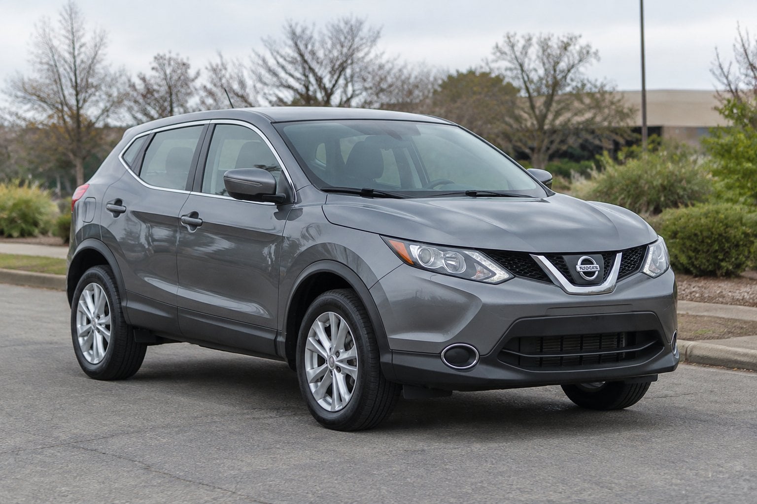 A gray compact SUV parked beside a suburban roadside under overcast skies.