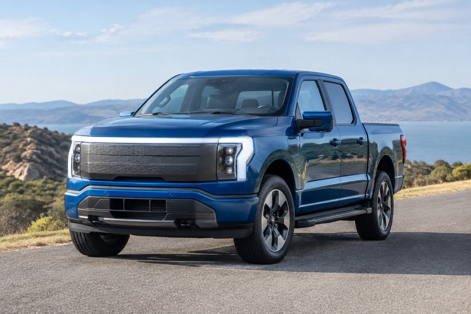 A modern electric pickup truck parked on a paved road beside an open landscape.