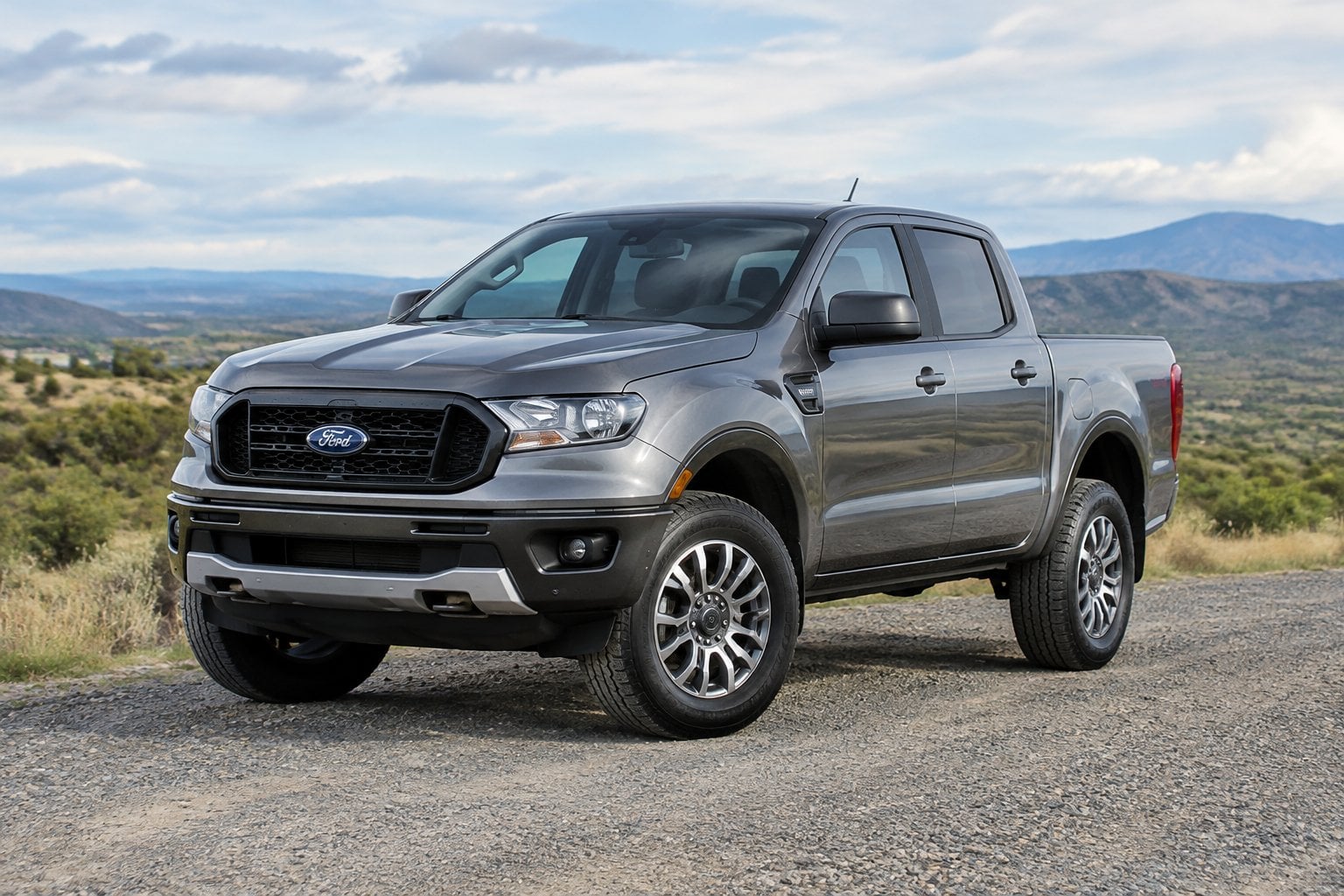 A pickup truck parked on a gravel road with hills in the background.